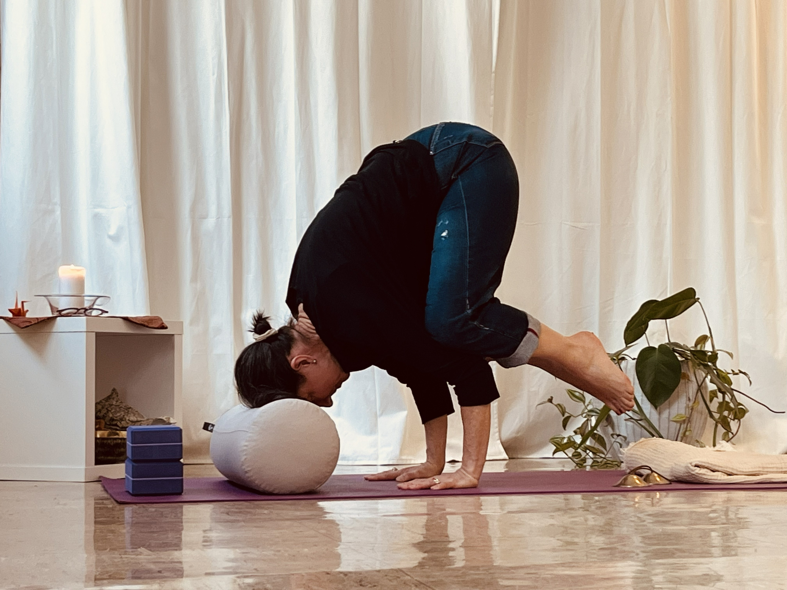 Yogapose Krähe mit dem Kopf auf einem dicken Bolster aufgestützt
